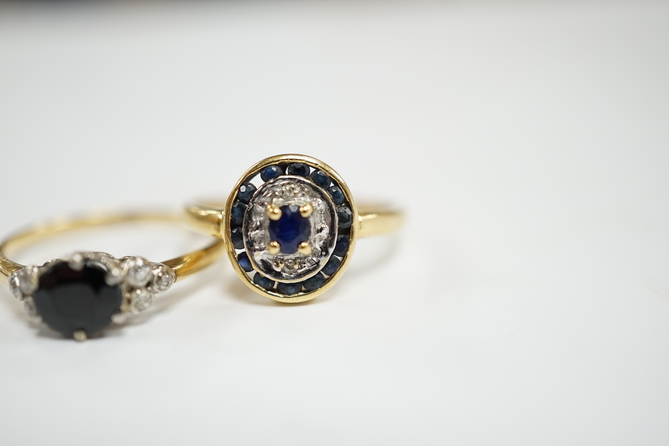 An 18ct, sapphire and diamond set seven stone ring, size P and a French 18k and sapphire set oval cluster ring, size O, gross weight 4.7 grams.